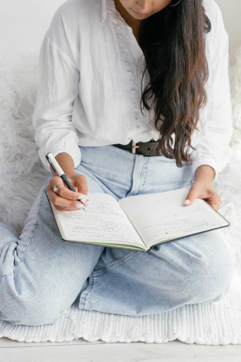 Young woman writing in a notebook indoors, reflecting on education and learning.